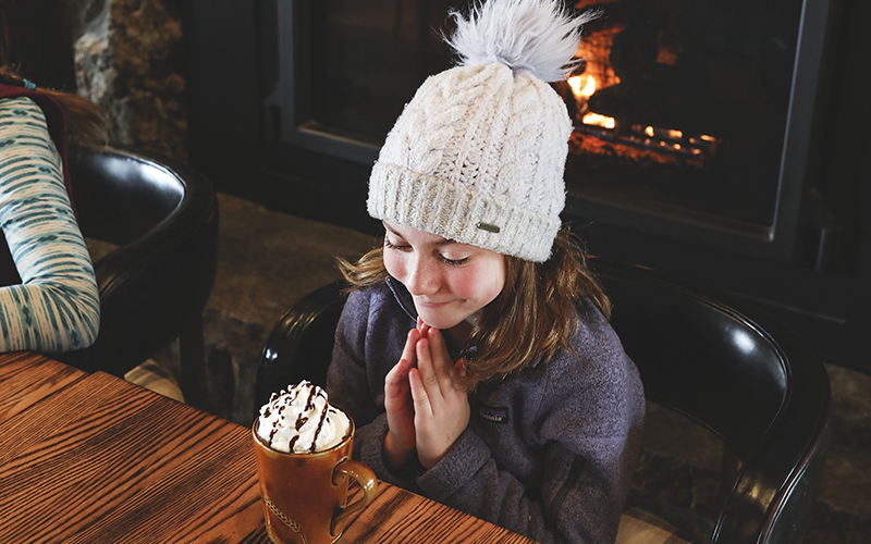 Girl with a mug of hot cocoa next to a fireplace. 