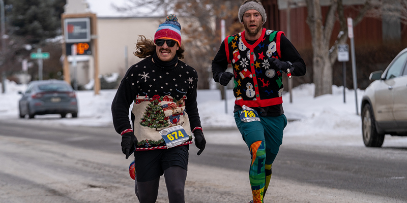 Two men in holiday sweaters running a fun run. 